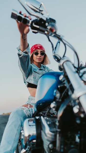 Donna sicura di sé che indossa un abito in denim e una bandana rossa mentre posa sulla sua moto