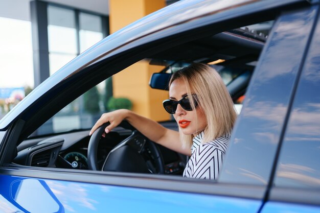 Donna sicura e bella in occhiali da sole. Vista posteriore della giovane femmina attraente in abbigliamento casual alla guida di un'auto