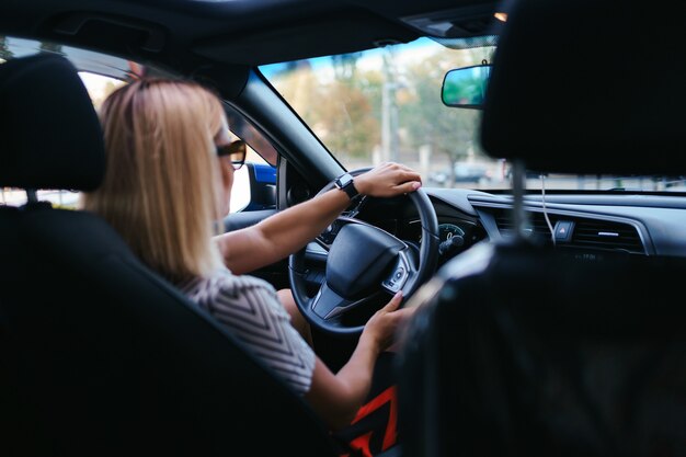 Donna sicura e bella in occhiali da sole. Vista posteriore della giovane femmina attraente in abbigliamento casual alla guida di un'auto