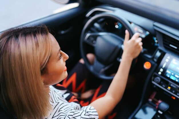 Donna sicura e bella in occhiali da sole. Vista posteriore della giovane femmina attraente in abbigliamento casual alla guida di un'auto