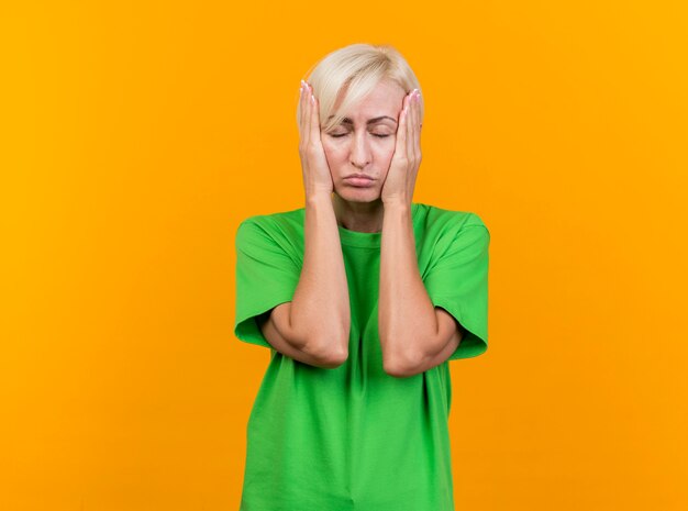 Donna slava bionda di mezza età stanca che mette le mani sul viso con gli occhi chiusi isolati sulla parete gialla con lo spazio della copia