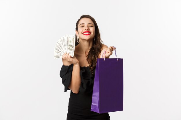 Donna soddisfatta e felice che gode dello shopping, che tiene borsa e denaro, sorridendo compiaciuta, in piedi su sfondo bianco.