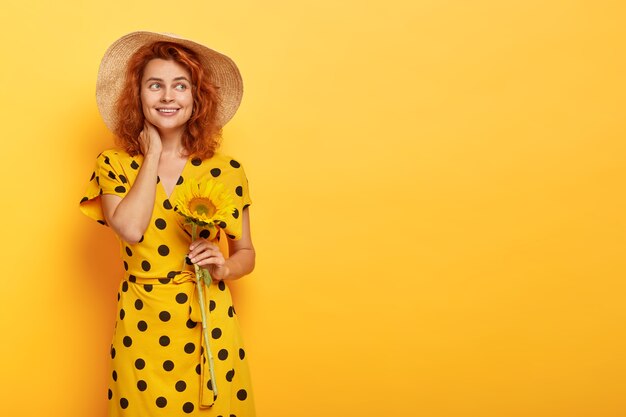 Donna sognante rossa in posa in abito giallo a pois e cappello di paglia