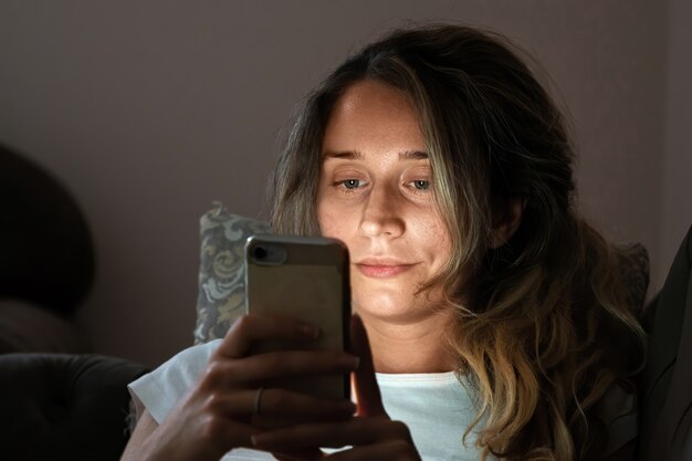 Donna sola che guarda il telefono cellulare nel letto di notte