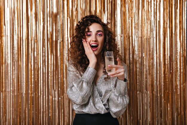 Donna sorpresa in camicetta d'argento che tiene un bicchiere di champagne