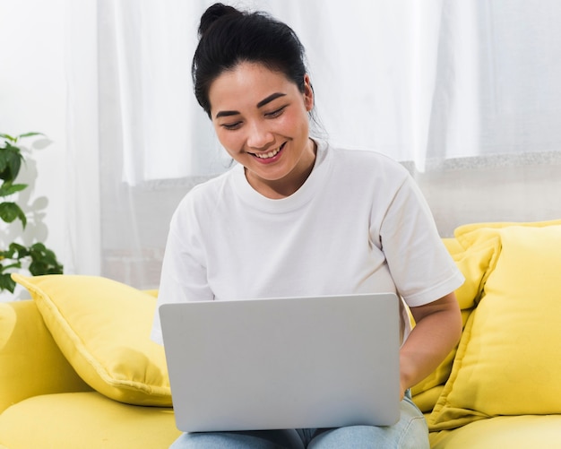 Donna sorridente a casa sul divano con il computer portatile