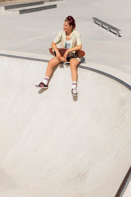 Donna sorridente a tutto campo con lo skateboard all'esterno