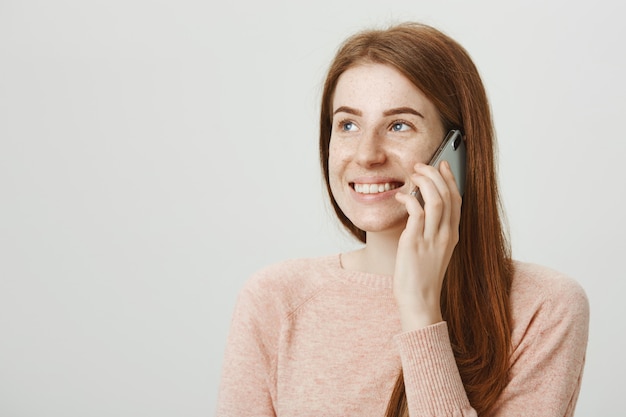 Donna sorridente attactive della testarossa che parla sul telefono cellulare