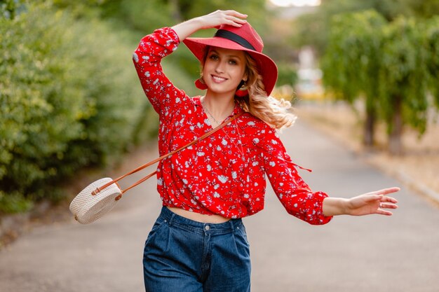 Donna sorridente bionda alla moda attraente carina in cappello rosso di paglia e camicetta vestito di moda estiva