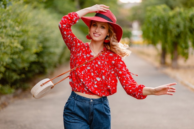 Donna sorridente bionda alla moda attraente carina in cappello rosso di paglia e camicetta vestito di moda estiva