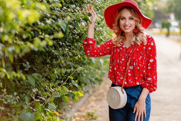 Donna sorridente bionda elegante abbastanza attraente in cappello rosso di paglia e vestito di moda estiva camicetta