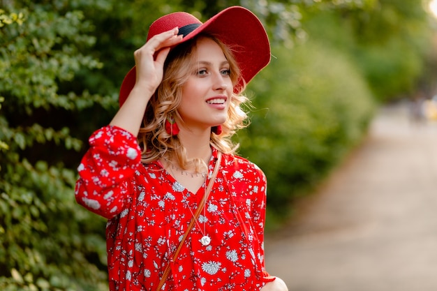 Donna sorridente bionda elegante abbastanza attraente in cappello rosso di paglia e vestito di moda estiva camicetta