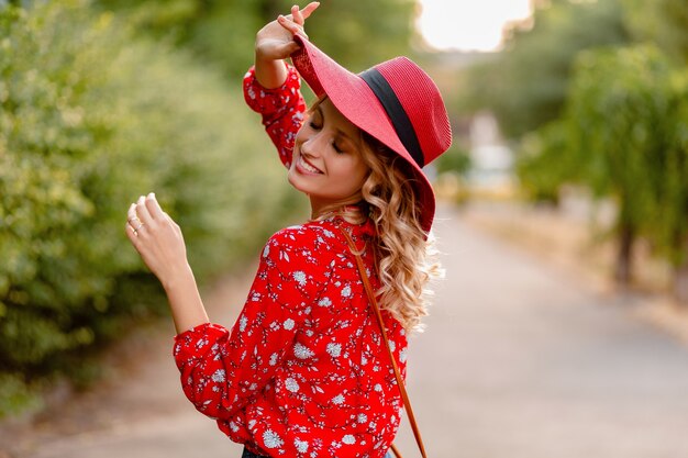 Donna sorridente bionda elegante abbastanza attraente in cappello rosso di paglia e vestito di moda estiva camicetta