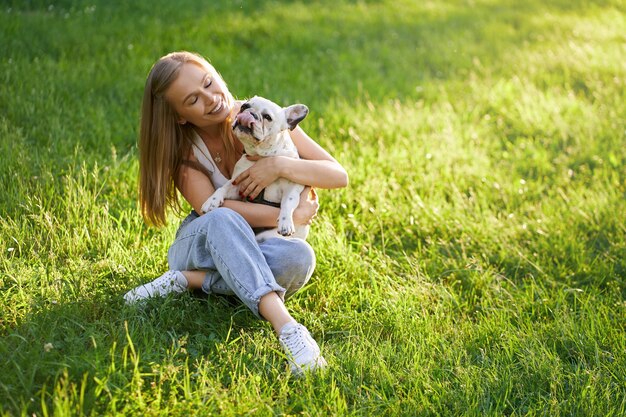 Donna sorridente che abbraccia bulldog francese sull'erba