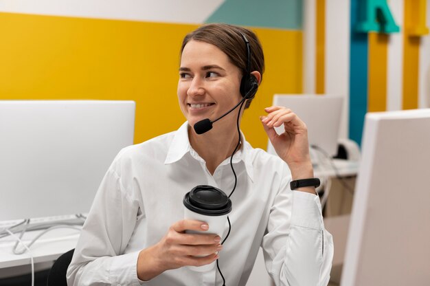 Donna sorridente che beve una tazza di caffè mentre lavora in un call center