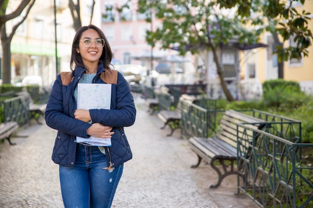 Donna sorridente che cammina all&#39;aperto e che tiene mappa piegata