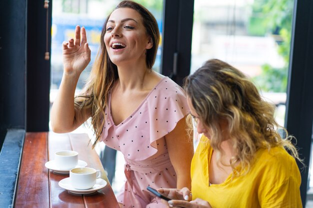 Donna sorridente che chiama cameriere e che si siede con l&#39;amico in caffè