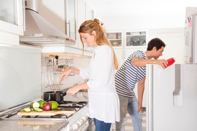 Donna sorridente che cucina le verdure mentre il suo marito che apre la porta del frigorifero