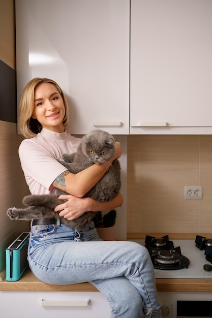 Donna sorridente che gioca con il gatto in cucina a casa.