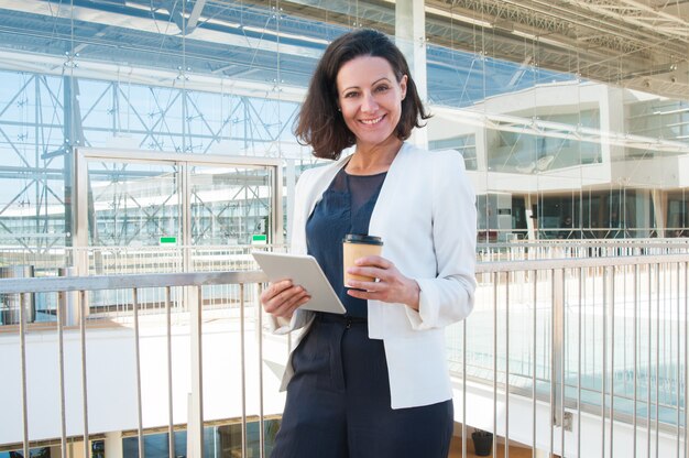 Donna sorridente che guarda l&#39;obbiettivo, tenendo compressa, caffè da asporto