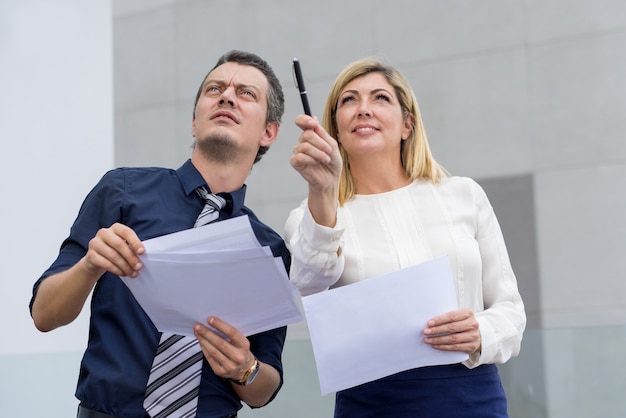 Donna sorridente che indica e che mostra collega maschio qualcosa all&#39;aperto.