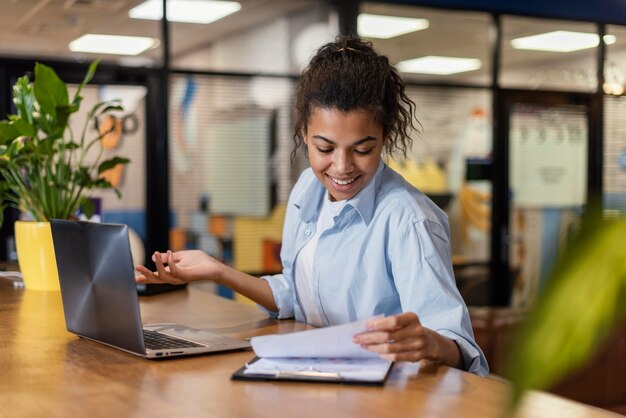 Donna sorridente che lavora in ufficio con documenti e laptop