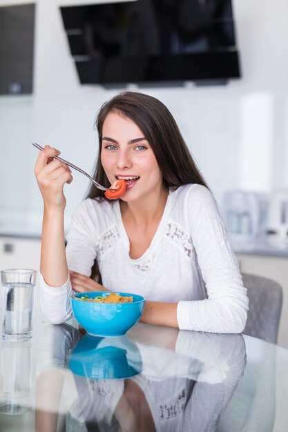 Donna sorridente che mangia un'insalata in cucina