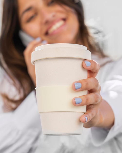 Donna sorridente che parla al telefono mentre si tiene la tazza di caffè