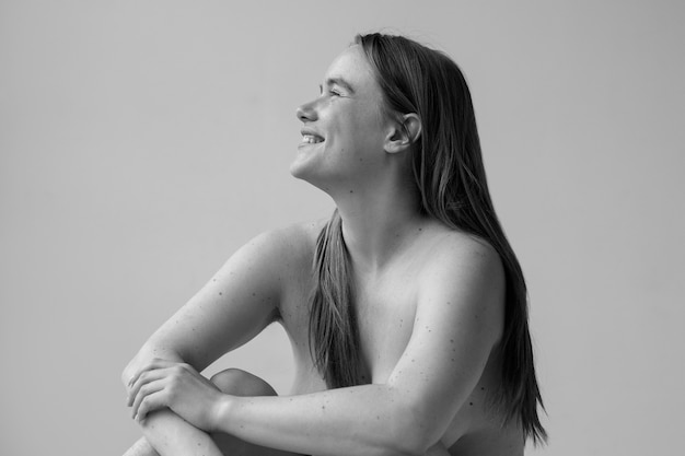 Donna sorridente che posa nuda nella vista laterale dello studio
