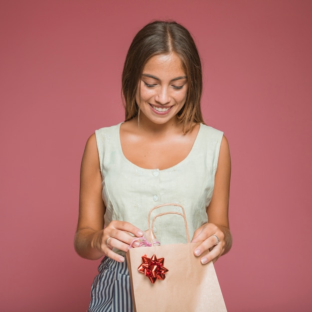 Donna sorridente che rimuove il contenitore di regalo dal sacchetto della spesa con l&#39;arco rosso