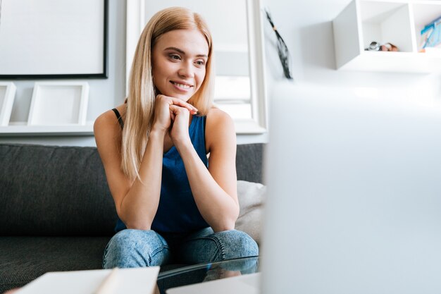 Donna sorridente che si siede sullo strato a casa e sul pensiero