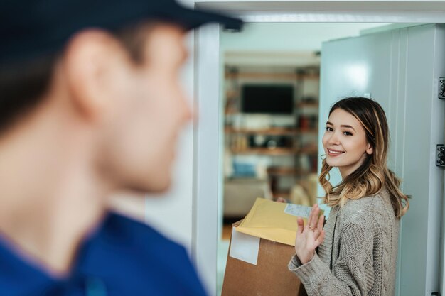 Donna sorridente che tiene i pacchi e saluta un corriere mentre si trova su una porta