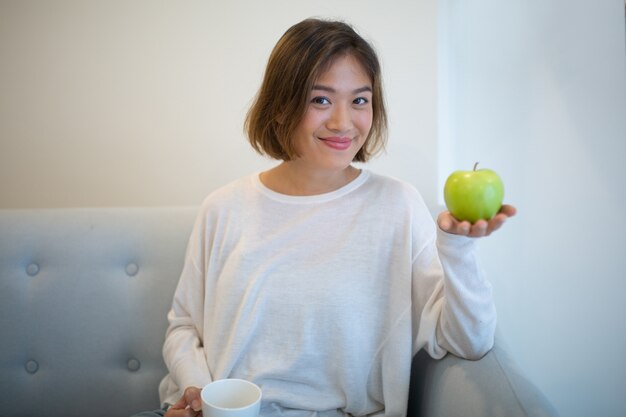 Donna sorridente che tiene mela verde e tazza di tè a casa