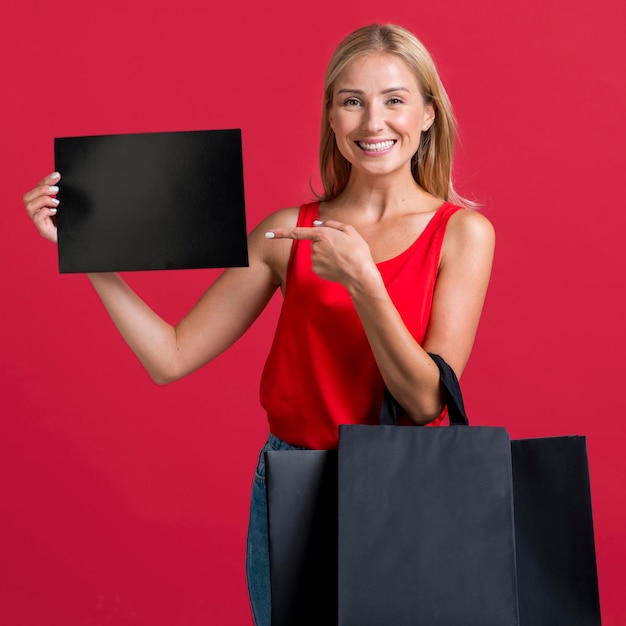 Donna sorridente che tiene segno in bianco e molti sacchetti della spesa