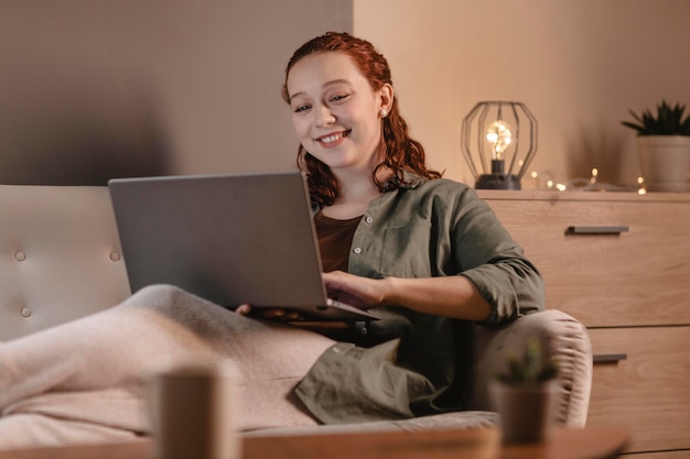 Donna sorridente che utilizza computer portatile a casa sul divano