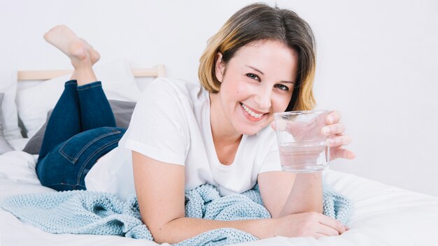 Donna sorridente con acqua sdraiata sul letto