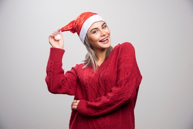 Donna sorridente con cappello da Babbo Natale in posa su sfondo grigio.