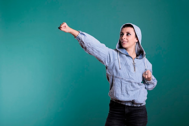 Donna sorridente con cappuccio in posa come supereroe mentre agisce come sorvolando sfondo isolato in studio. Modello che fa il gesto del difensore della giustizia che ha il potere di essere pronto a salvare il mondo, serio exp