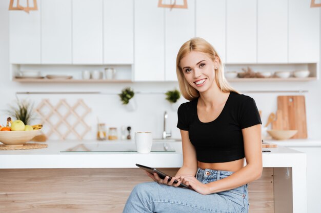 Donna sorridente con il computer della compressa in cucina