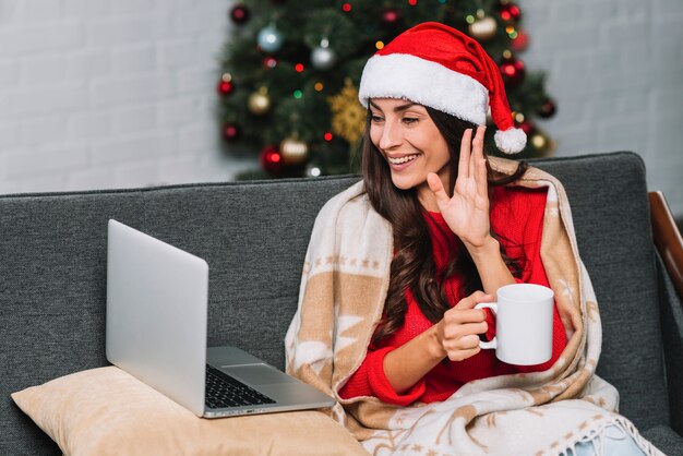 Donna sorridente con la tazza vicino al computer portatile sul divano