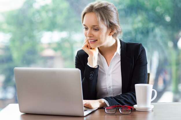 Donna sorridente con la testa appoggiata su una mano guardando un computer portatile