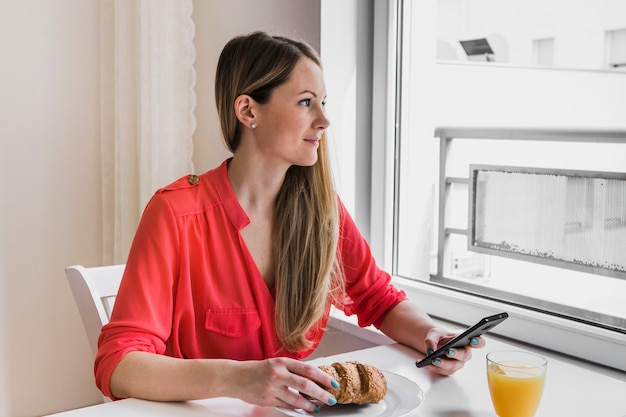 Donna sorridente con lo smartphone che osserva fuori finestra