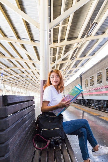 Donna sorridente con mappa, zaino e macchina fotografica sul banco