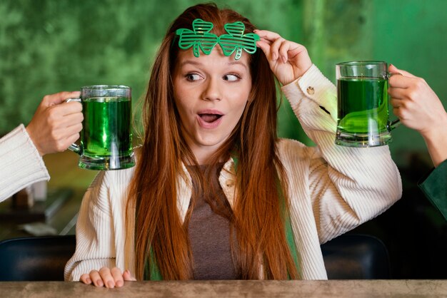 Donna sorridente con occhiali trifoglio che celebra st. patrick's day al bar con bevande