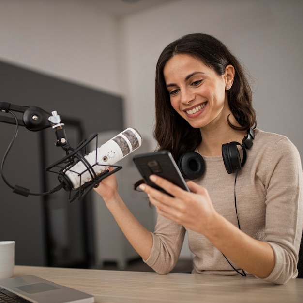 Donna sorridente con smartphone e microfono in uno studio radiofonico