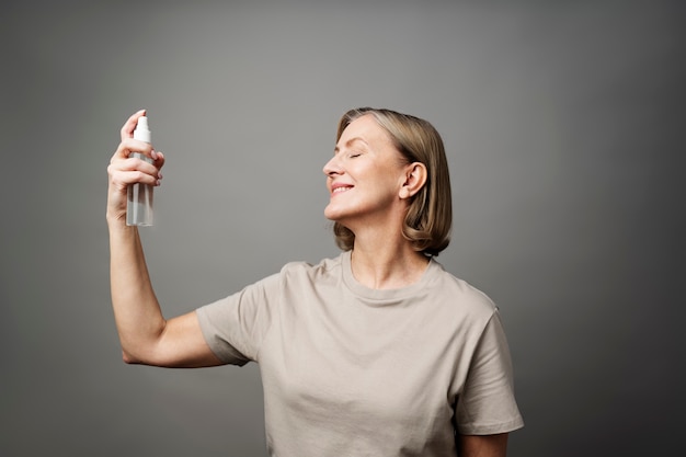 Donna sorridente del colpo medio che applica lo spruzzo