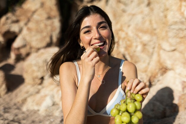 Donna sorridente del colpo medio che mangia l'uva