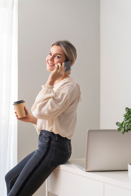 Donna sorridente del colpo medio che parla sul telefono