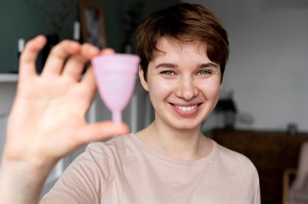 Donna sorridente del colpo medio che tiene la tazza mestruale