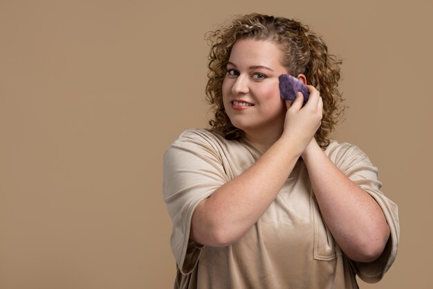 Donna sorridente del colpo medio che usa lo strumento gua sha